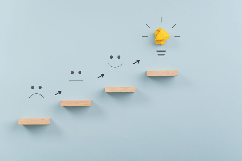 Business vision, idea and development concept - steps made of wooden pegs leading to a lightbulb. Over light blue background.